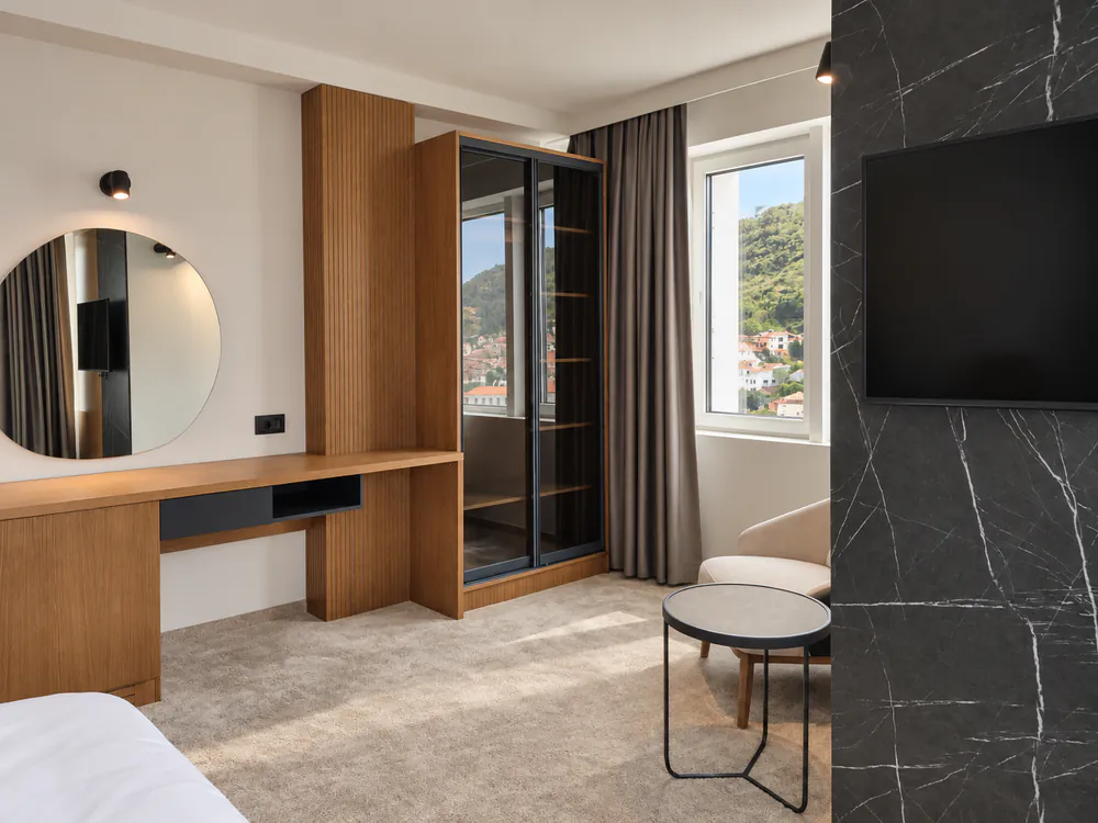 Room with oak desk and round mirror, glass-fronted wardrobe, armchair by the window and a black marble TV wall