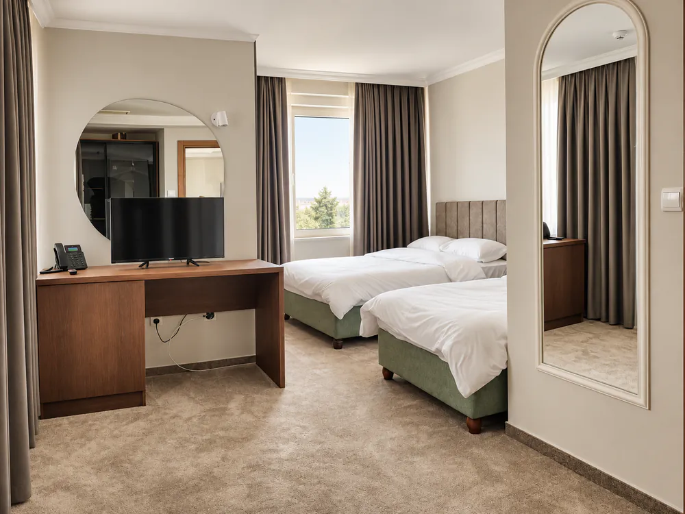 Twin room with two single beds on sage-green bases, oak desk with TV, round mirror and a tall arched mirror